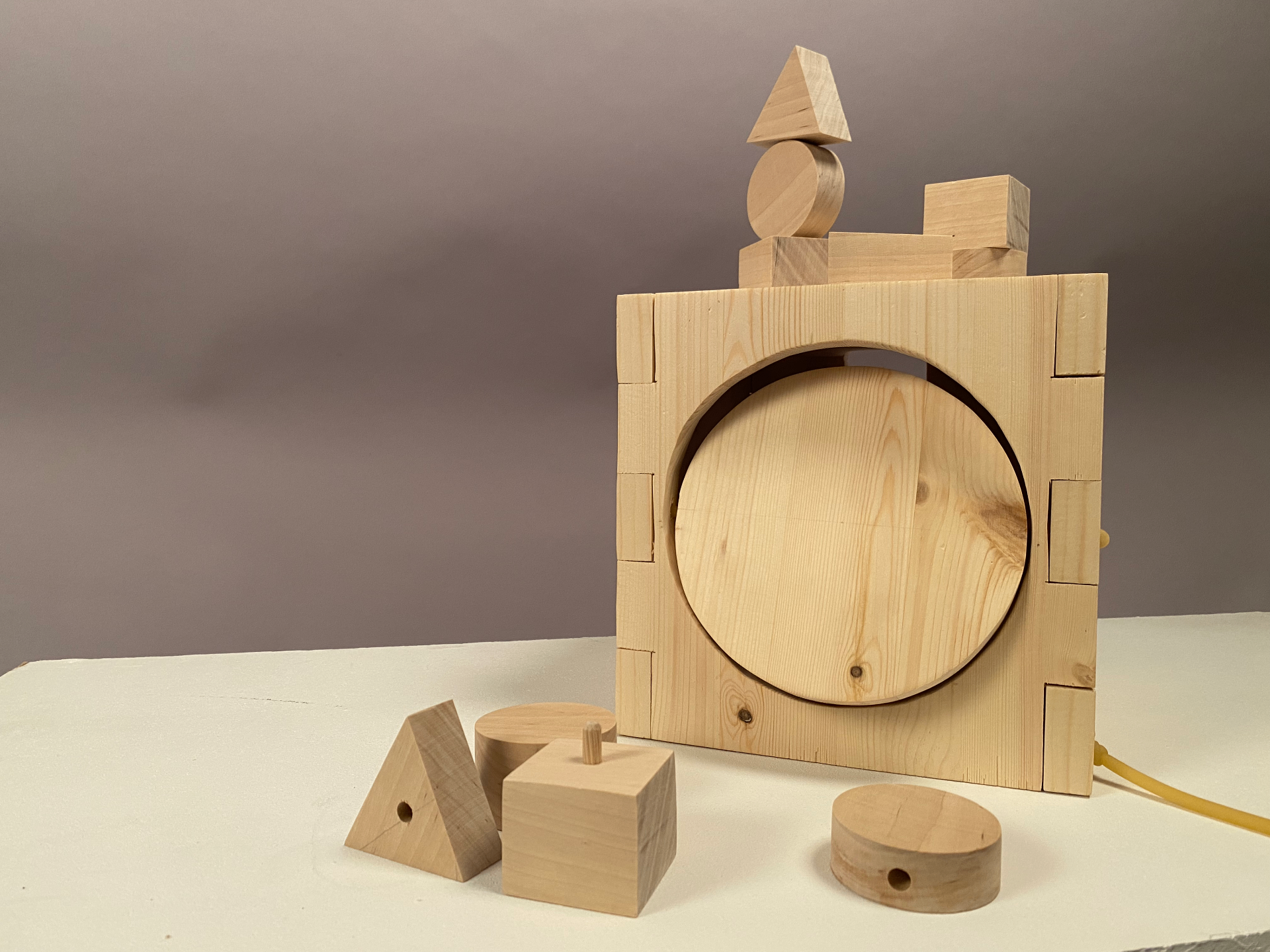 Studio photo of the wooden activity box showing the large circular rotating door on the front, with wooden shape blocks stacked on top of the box.